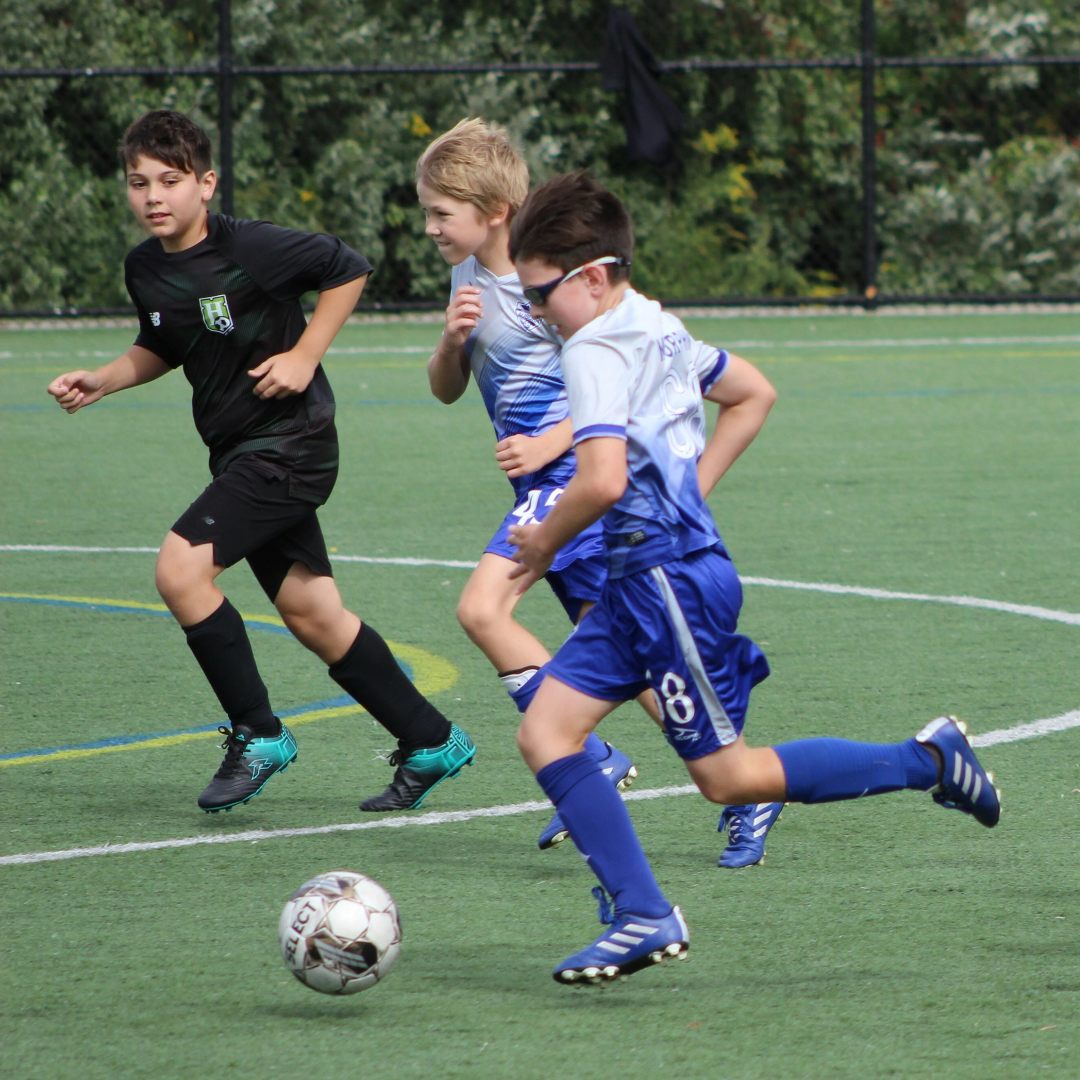 Children playing soccer on a green field with trees in the background